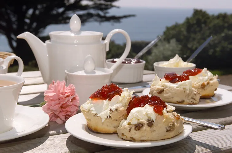 Traditional English Afternoon Tea setup with teacups, scones, and sandwiches.
